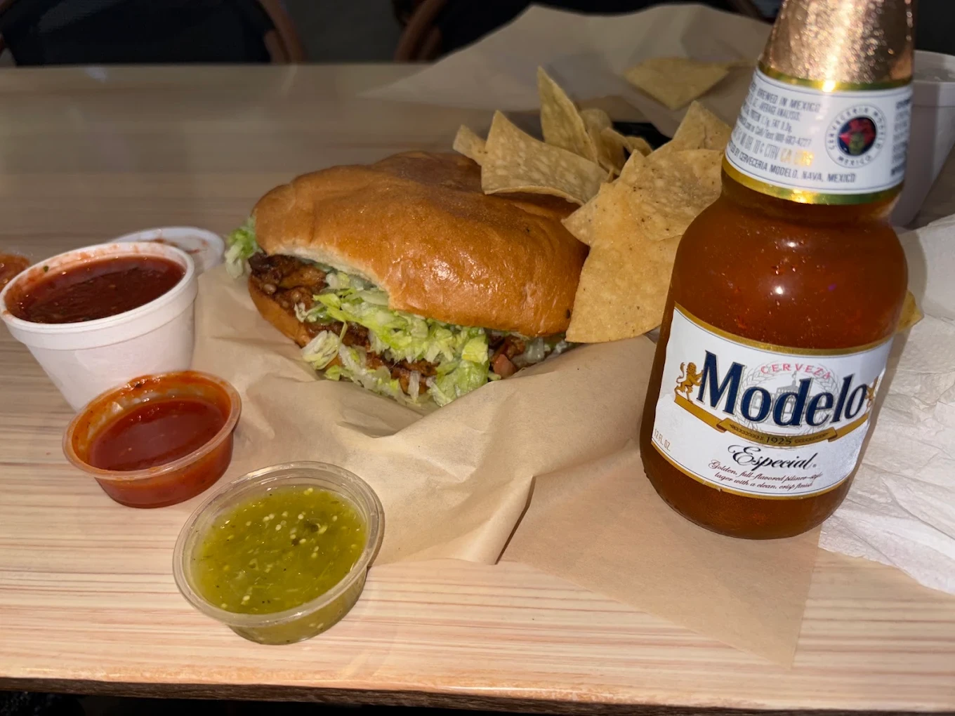 A torta sandwich with chips, salsa and a bottled drink
