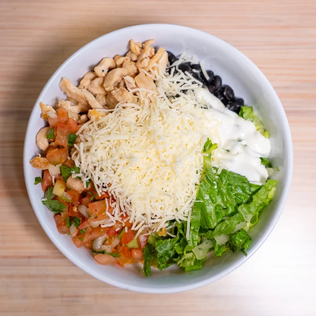 A burrito bowl layered with rice, beans, lettuce and cheese