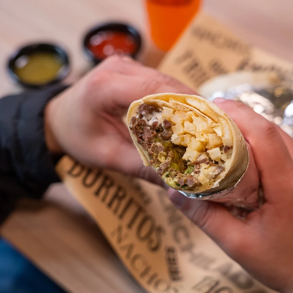 A hand holding a cut burrito filled with steak and fries