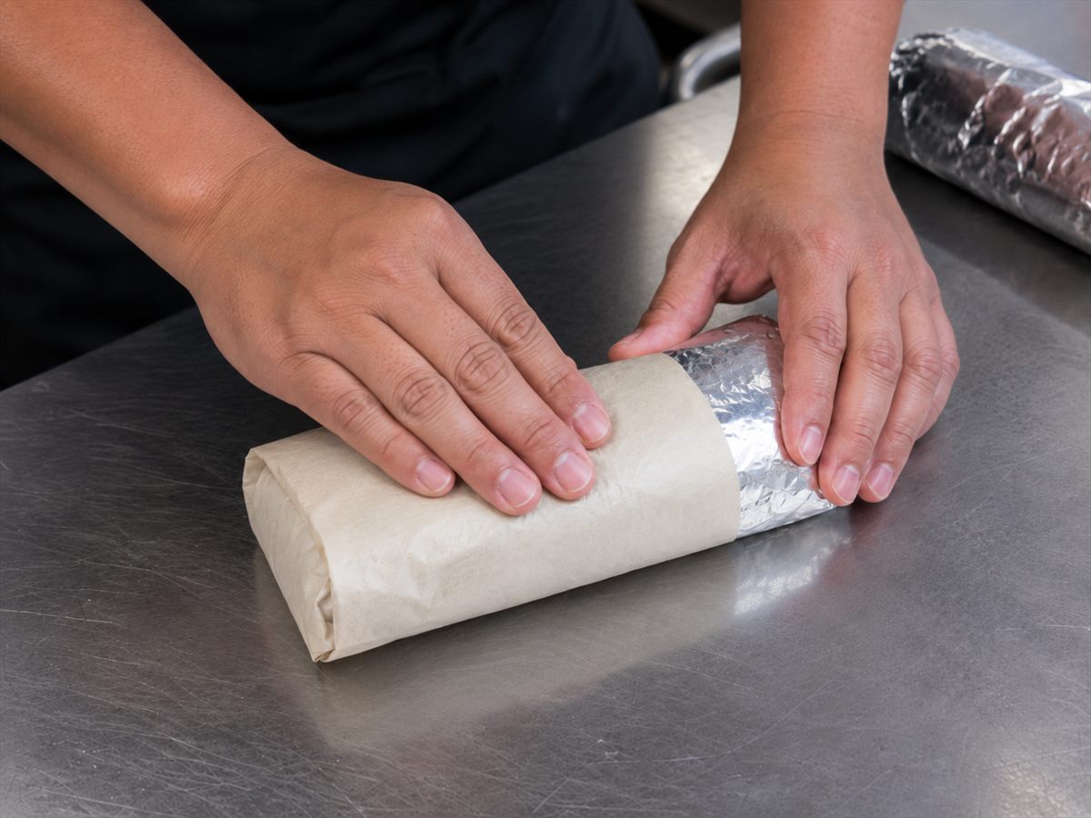 A finished burrito being wrapped in paper and foil